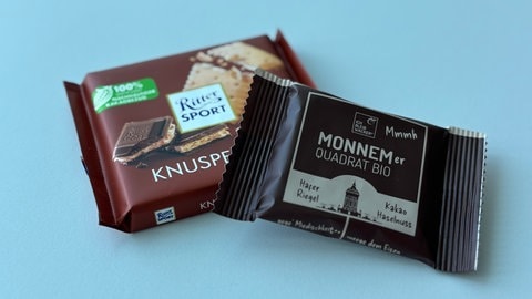 Eine Tafel Ritter Sport liegt neben einem Haferriegel von Wacker