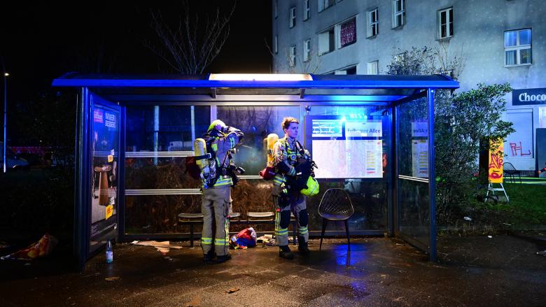Feuerwehrmänner stehen während der Silvesternacht nach einer Brandbekämpfung im Britzer Weg an einer Bushaltestelle. (Quelle: Picture Alliance/Sebastian Gollnow)