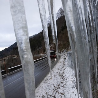 Ein Bus, der auf einer Landstraße fährt, ist durch mehrere lange Eiszapfen hindurch zu sehen.