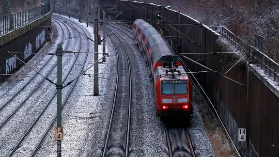 Ein Regionalzug der Deutschen Bahn fährt auf verschneiten Schienen.