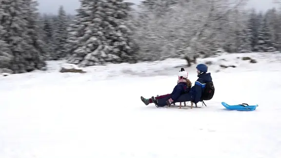 Zwei Menschen rodeln auf einem schneebedeckten Rodelberg in Torfhaus.