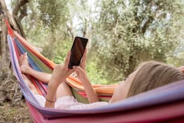 Eine Frau liegt in einer Hängematte und hat ein Handy in der Hand.