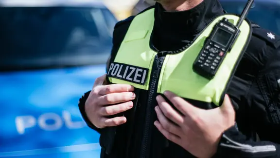 Ein Polizist, der seine Hände unter die Schutzweste der Uniform gesteckt hat.