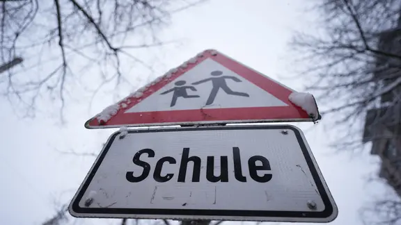 Schnee liegt auf einem Verkehrsschild und Hinweisschild mit der Aufschrift "Schule".