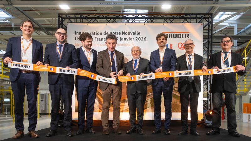 Eine Gruppe von acht Personen steht auf einer Bühne und hält ein Band bei einer Eröffnungszeremonie.