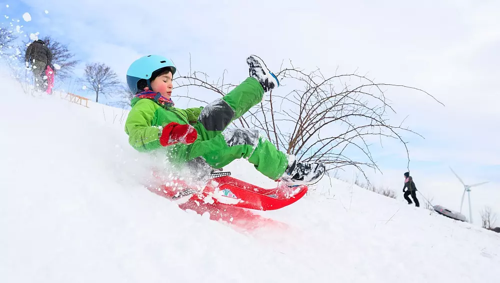 Ein Kind fährt mit seinem Schlitten am Kronsberg. - © Julian Stratenschulte/dpa