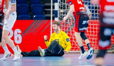 Ein Handballtorwart im gelben Trikot sitzt mit geballter Faust auf dem Boden und feiert, während Spieler in roten und weißen Trikots während des THW Kiel Handball-Derbys in der EHF European League Saison 2025/2026 in der Nähe laufen.