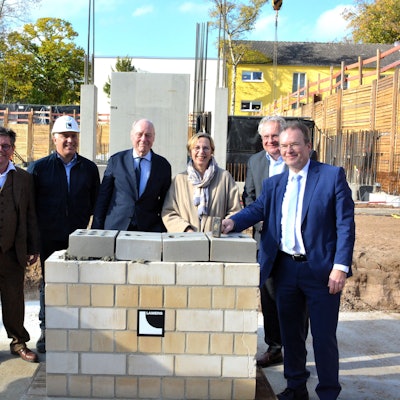 Fünf Männer und eine Frau stehen hinter einer hüfthoch gemauerten Wand.