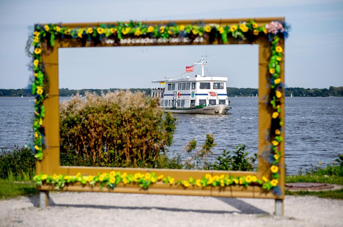 Postkartenmotiv in Bad Zwischenahn: Das Ausflugsschiff „Ammerland“ ist bei sonnigem Wetter auf dem Zwischenahner Meer unterwegs, während im Vordergrund dekorativ ein überdimensionaler Bilderrahmen steht und das Schiff in Szene setzt.