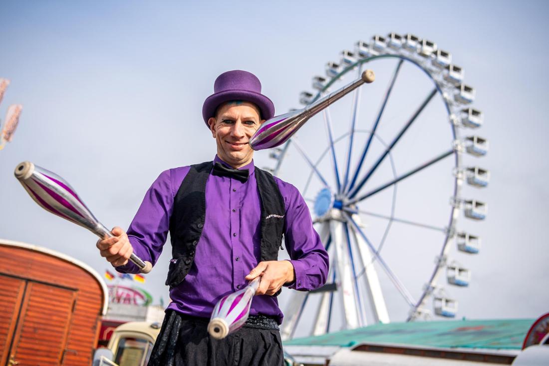 In Oldenburg steht ein Jongleur mit lila Hemd und schwarzer Hose vor dem Riesenrad im Hintergrund auf dem 415. Kramermarkt im Jahr 2022. Der nächste Markt findet vom 29. September bis 8. Oktober 2023 statt.