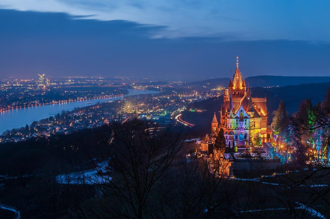 Schloss Drachenburg von der Seite bei Nacht mit Stadtpanorama