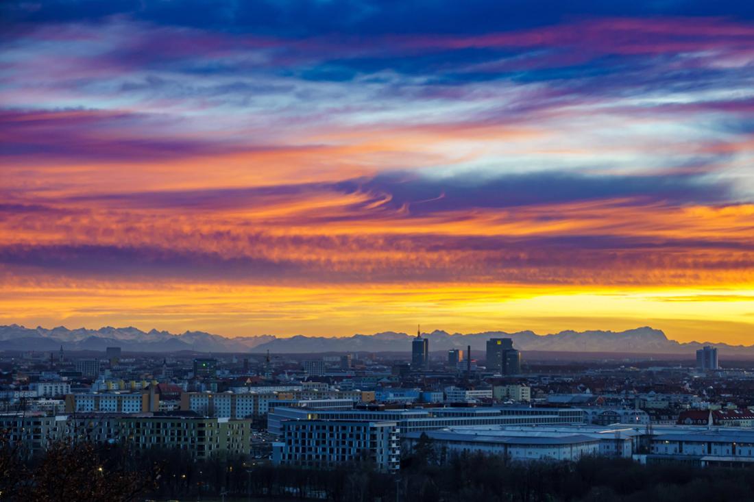 Farbenspiel durch Abendrot: Die Skyline von München samt Bergpanorama im Hintergrund.