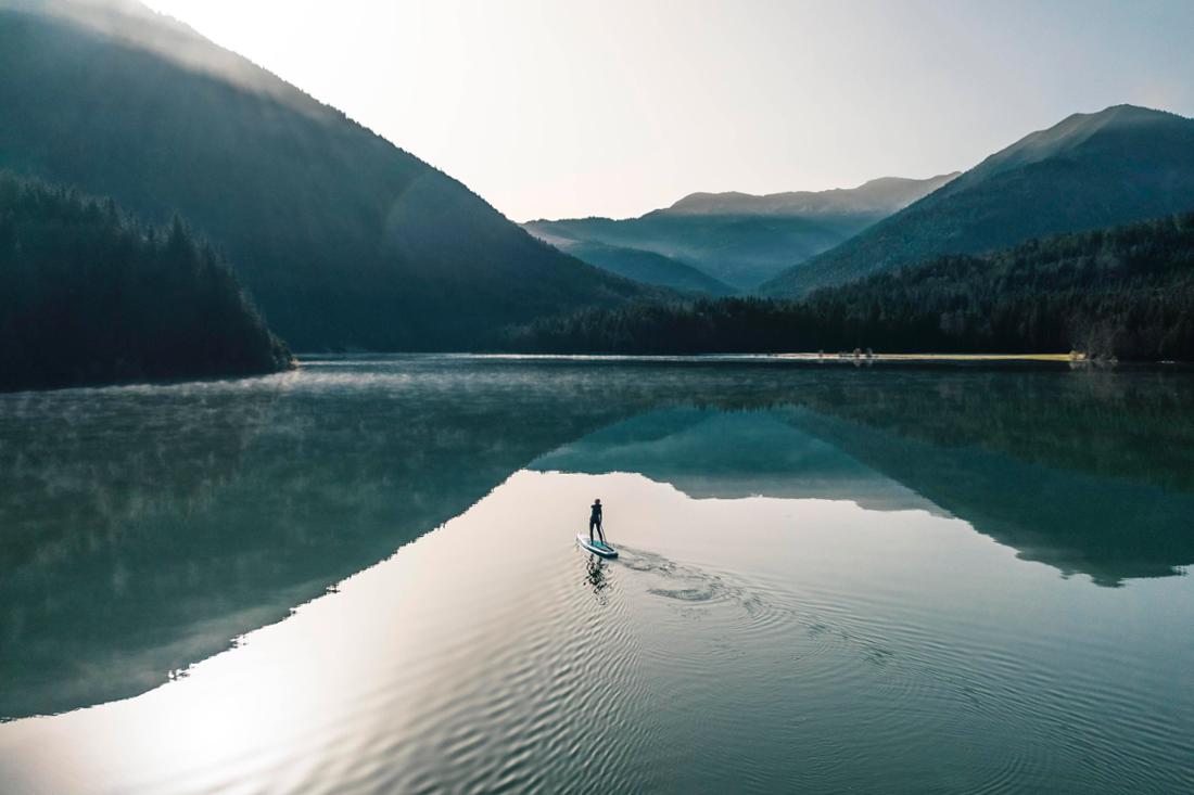 Perfekte Spiegelung auf dem Sylvensteinsee: ein Stand-up-Paddler gleitet einsam über das Wasser. 