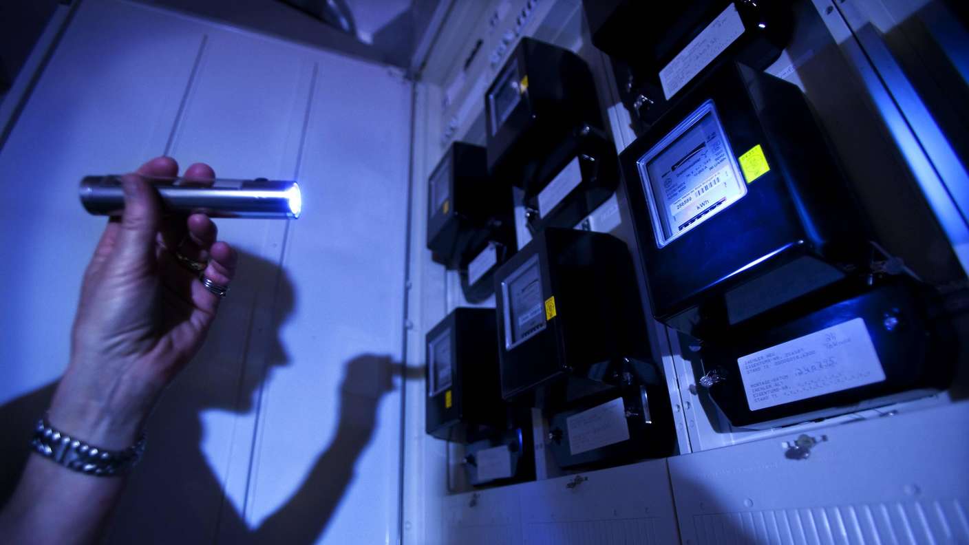 Eine Hand, die eine Taschenlampe hält, richtet den Lichtstrahl auf einen Stromzähler