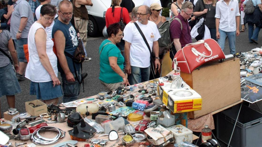 Viele Menschen auf einem Flohmarkt. Im Vordergrund ein Stand.