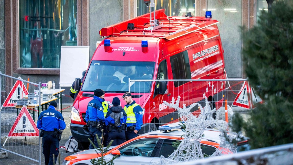 Ein Rettungswagen steht hinter einer Absperrung, davor stehen Einsatzkräfte und unterhalten sich.