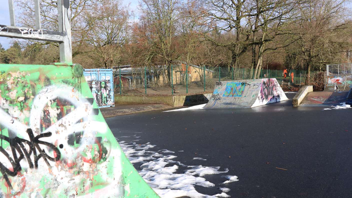 eine Skateranlage, im Hintergrund hinter einem Zaun ist ein Schulbau erkennbar  