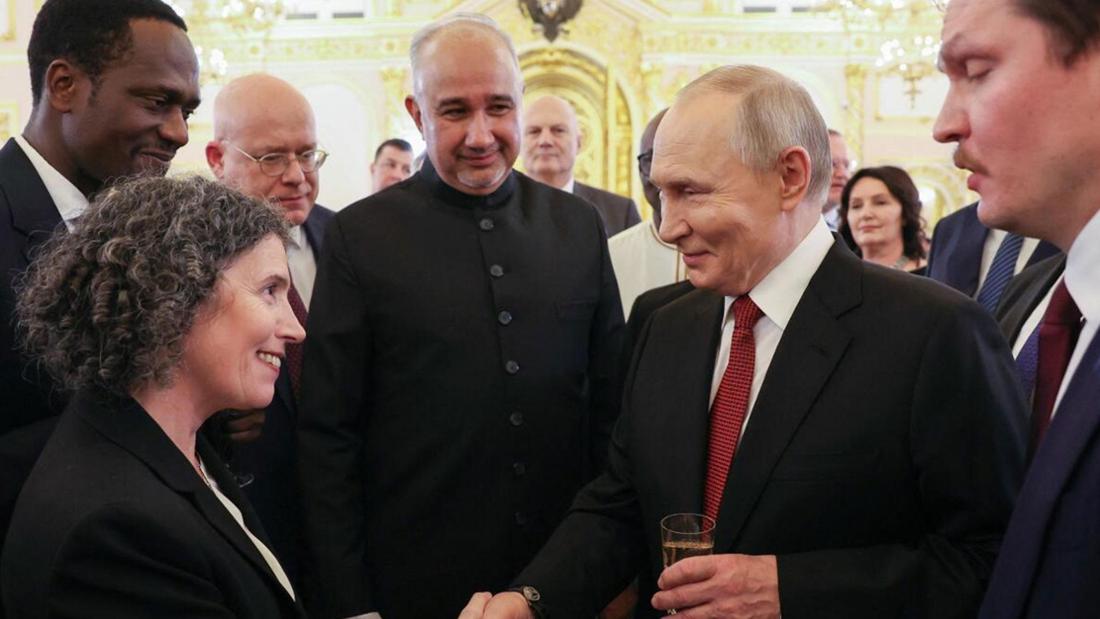 Wladimir Putin schüttelt einer Frau die Hand, mehrere Männer stehen drumherum