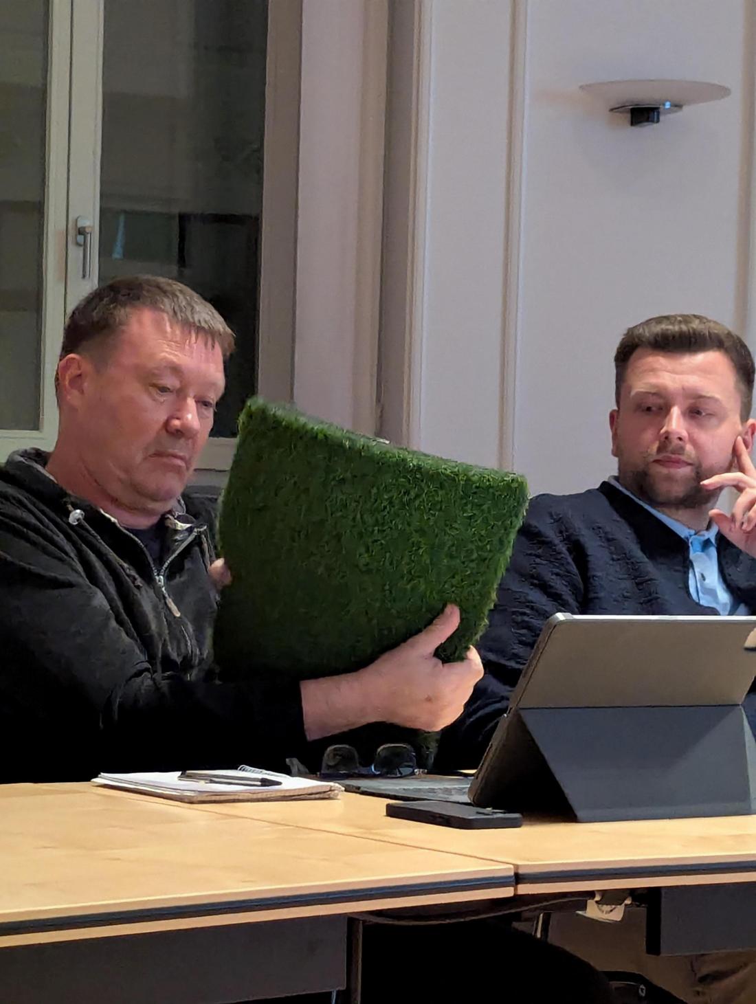 Zwei Männer, die ein Stück Kunstrasen betrachten 