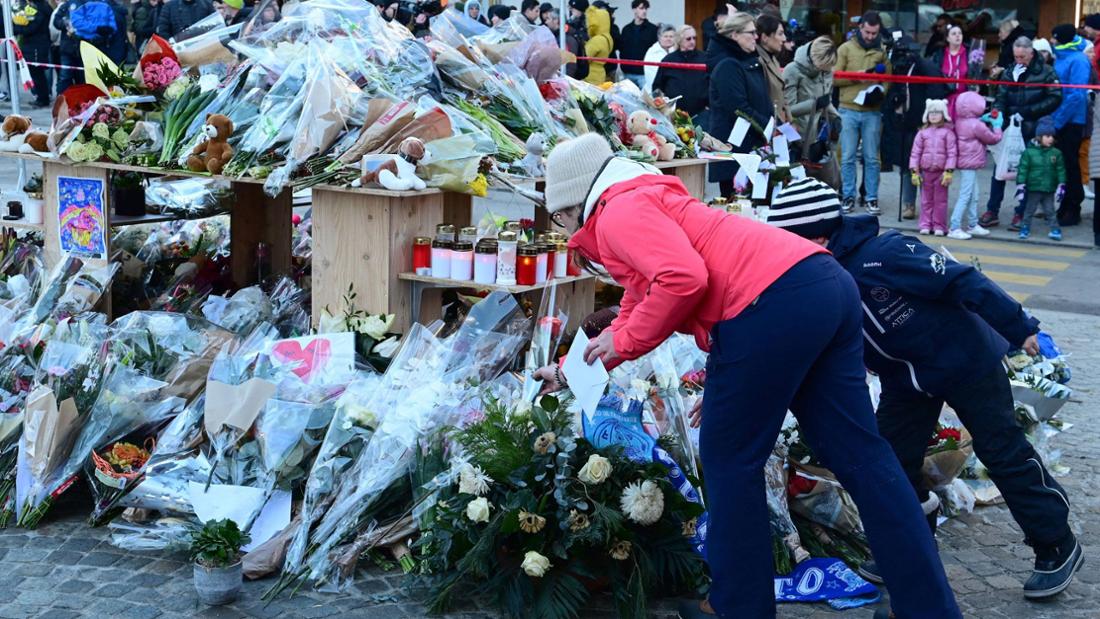 Menschen legen Blumen und Kerzen rund um einen Holztisch im Freien nieder