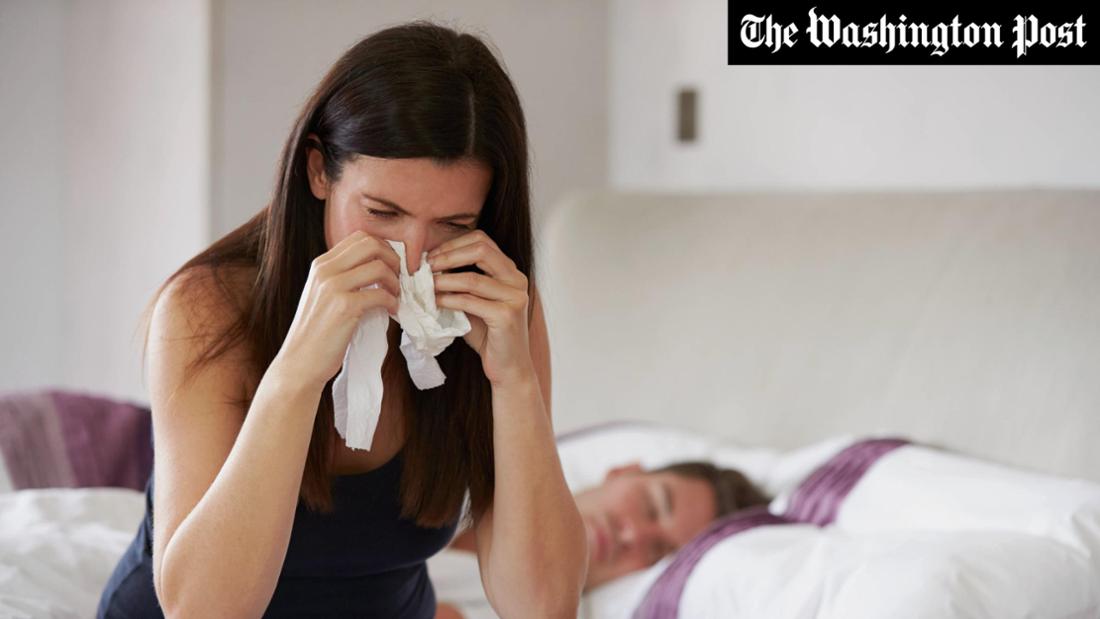 Eine Frau leidet unter ihrer Erkältung, während ihr Mann schläft (Symbolbild).