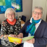 Die Hertenerinnen Beate Wanjek (links) und Ursula Schneider stehen in einem Wohnzimmer und halten ein Kinderbuch in ihren Händen.