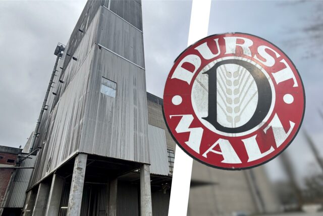 Ein graues, modernes Gebäude mit Holzfassade steht im Vordergrund, daneben ein rundes Logo mit der Aufschrift „DURST MALZ“.