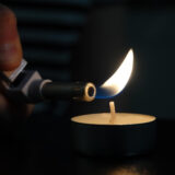 Ein Teelicht wird mit einem Feuerzeug angezündet. Drumherum ist es dunkel.