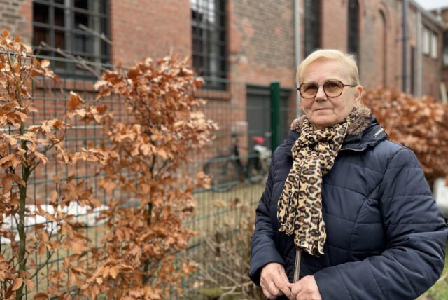 Die Dortmunderin Eugenia Kostrzewa steht am Zaun ihres Grundstücks in Dorstfeld. Im Hintergrund: das Bürgerhaus des Stadtteils.