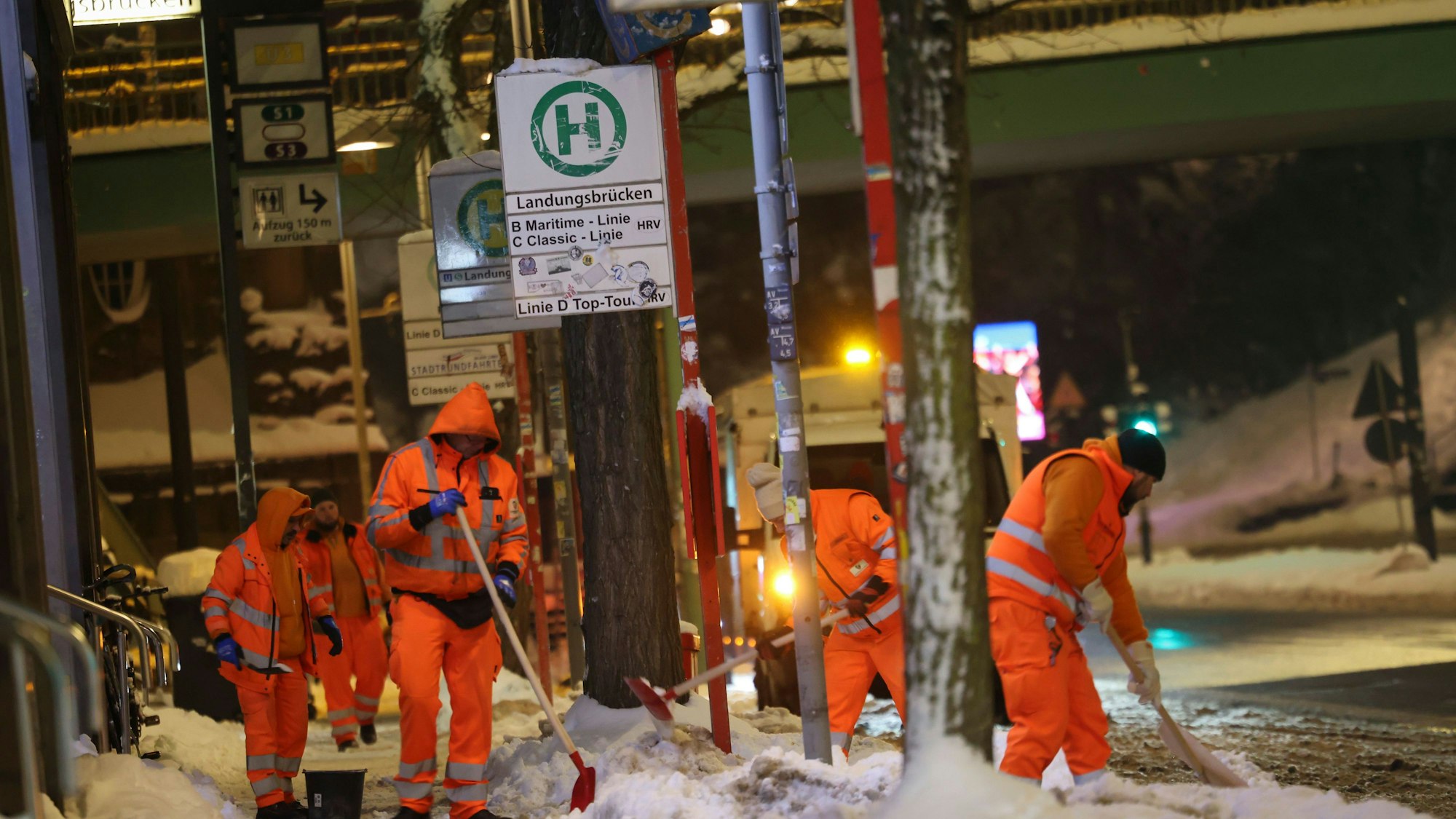Das Bild zeigt Mitarbeiter der Stadtreinigung Hamburg die Schnee und Eis von der Bushaltestelle an den Landungsbrücken räumen. Foto: Christian Charisius/dpa