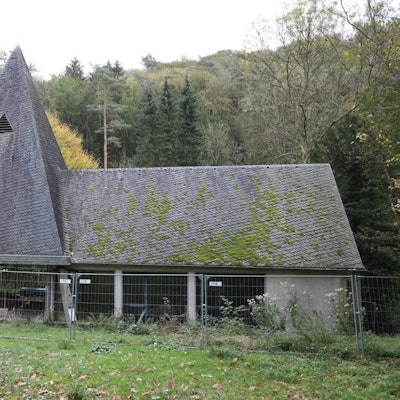 Eine Kapelle mit Turm und Trauerhalle, auf das Schieferdach wächst zum Teil Moos.