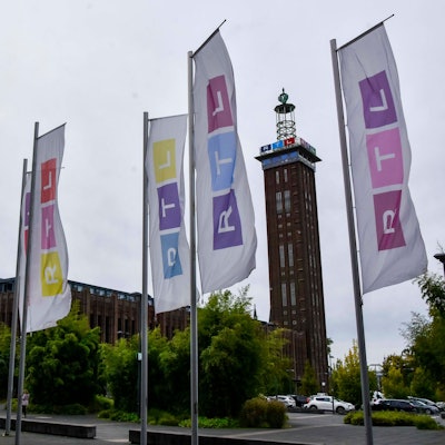 Der Kölner Messe Turm, davor bunte Fahnen mit dem RTL Logo in Deutz am Picassoplatz
