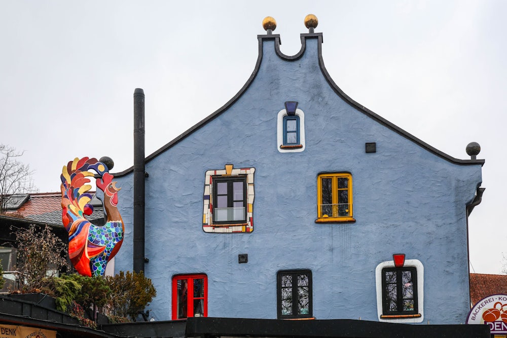 An der Front des Bäckereigebäudes erkennt man deutlich den Stil von Hundertwasser. Die Gockel-Skulptur stammt vom Dachauer Künstler Heinz Eder.