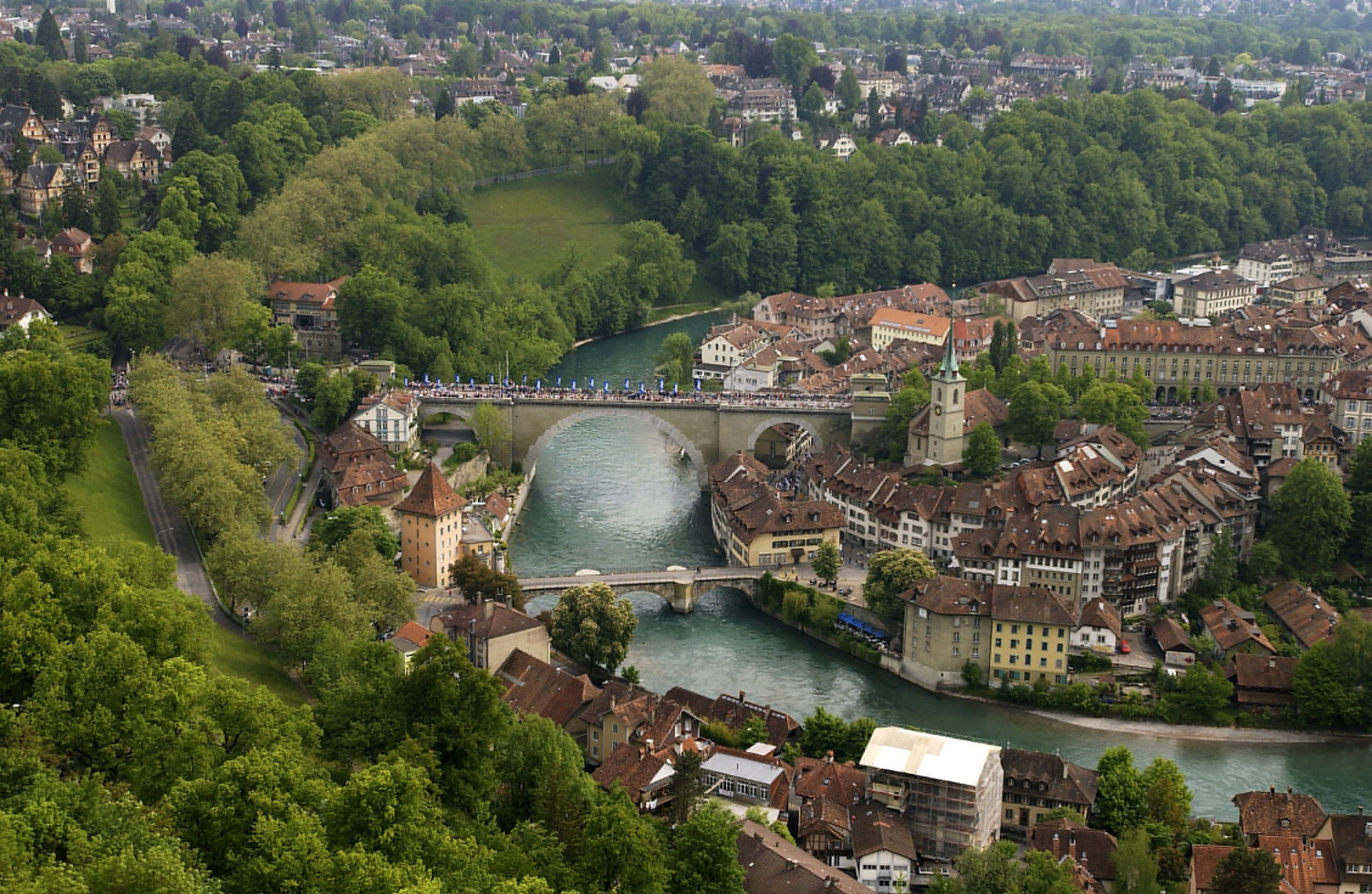 Luftaufnahme der Unteren Altstadt von Bern mit der Nydeggbrücke über die Aare, umgeben von grüner Landschaft.
