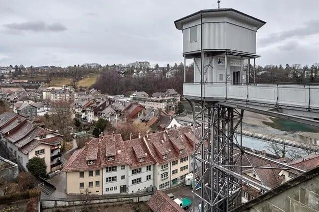 Ansicht auf eine historische Stadt mit traditionellem roten Ziegeldach, einem modernen Aussichtsturm und einem Fluss im Hintergrund.