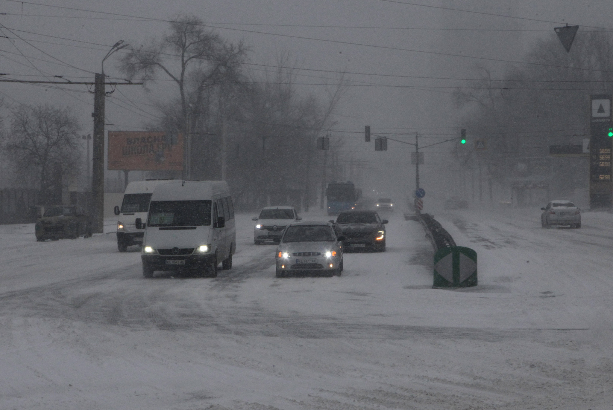 Autos fahren auf einer verschneiten Strasse im Winter in Dnipro, Ukraine. Schnee bedeckt die Fahrbahn, Sicht verschlechtert.
