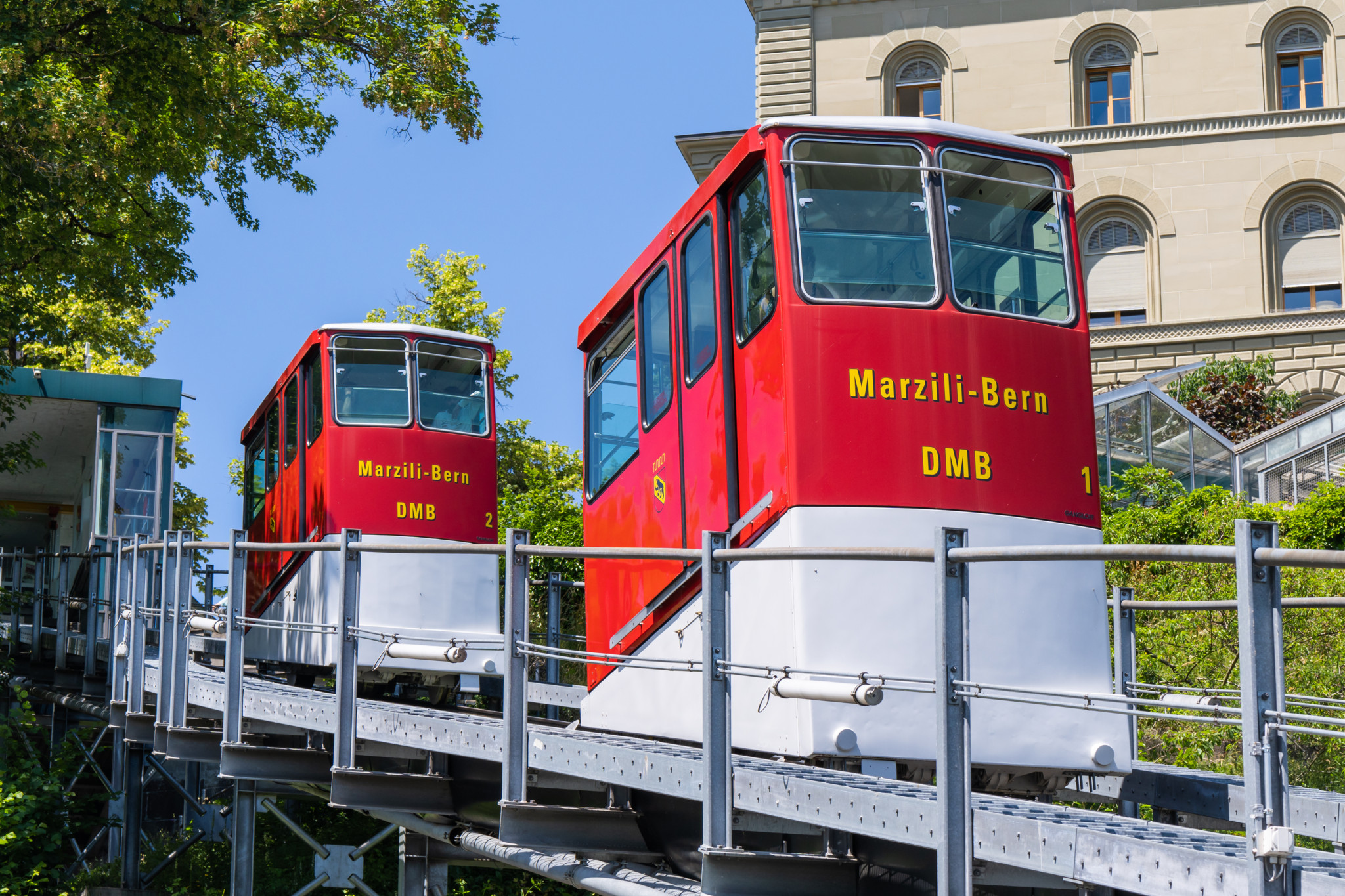 Die rote Marzilibahn in Bern auf ihrem Weg nach oben, mit zwei Wagen vor einem blauen Himmel.