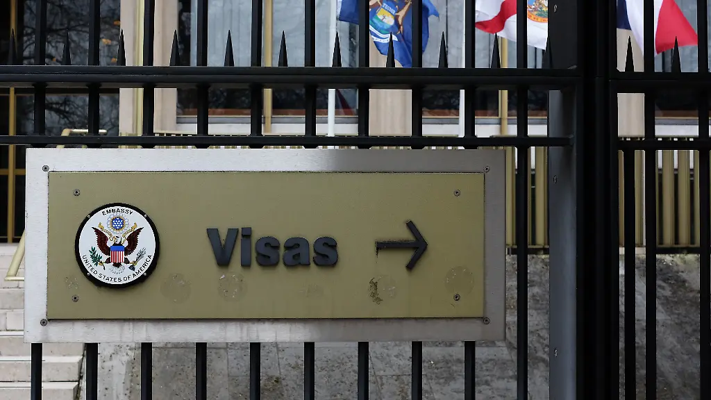 Ein-Schild-mit-der-Aufschrift-Visas-und-das-Grosse-Siegel-der-Vereinigten-Staaten-sind-an-einem-Zaun-vor-dem-Gebaeude-der-Botschaft-der-USA-am-Grosvenor-Square-in-London-angebracht-fotografiert-am-17-03-2017-in-London-Grossbritannien-Im-Hintergrund-einige-Flaggen-der-50-amerikanischen-Bundesstaaten