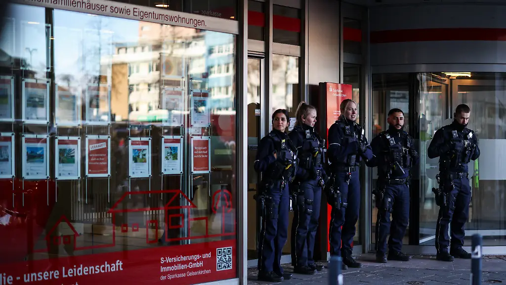 Einsatzkraefte-der-Polizei-stehen-vor-der-Sparkassenfiliale-im-Stadtteil-Buer-Nach-dem-Einbruch-in-den-Tresorraum-der-Bank-fordern-besorgte-Kunden-Informationen-Aufgrund-der-Situation-bleibe-die-Filiale-auch-am-Dienstag-geschlossen-wie-die-Polizei-mitteilte