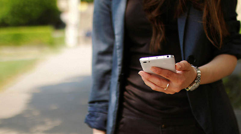 Bildbeschreibung: Eine Frau die ein Handy in der Hand hält.
