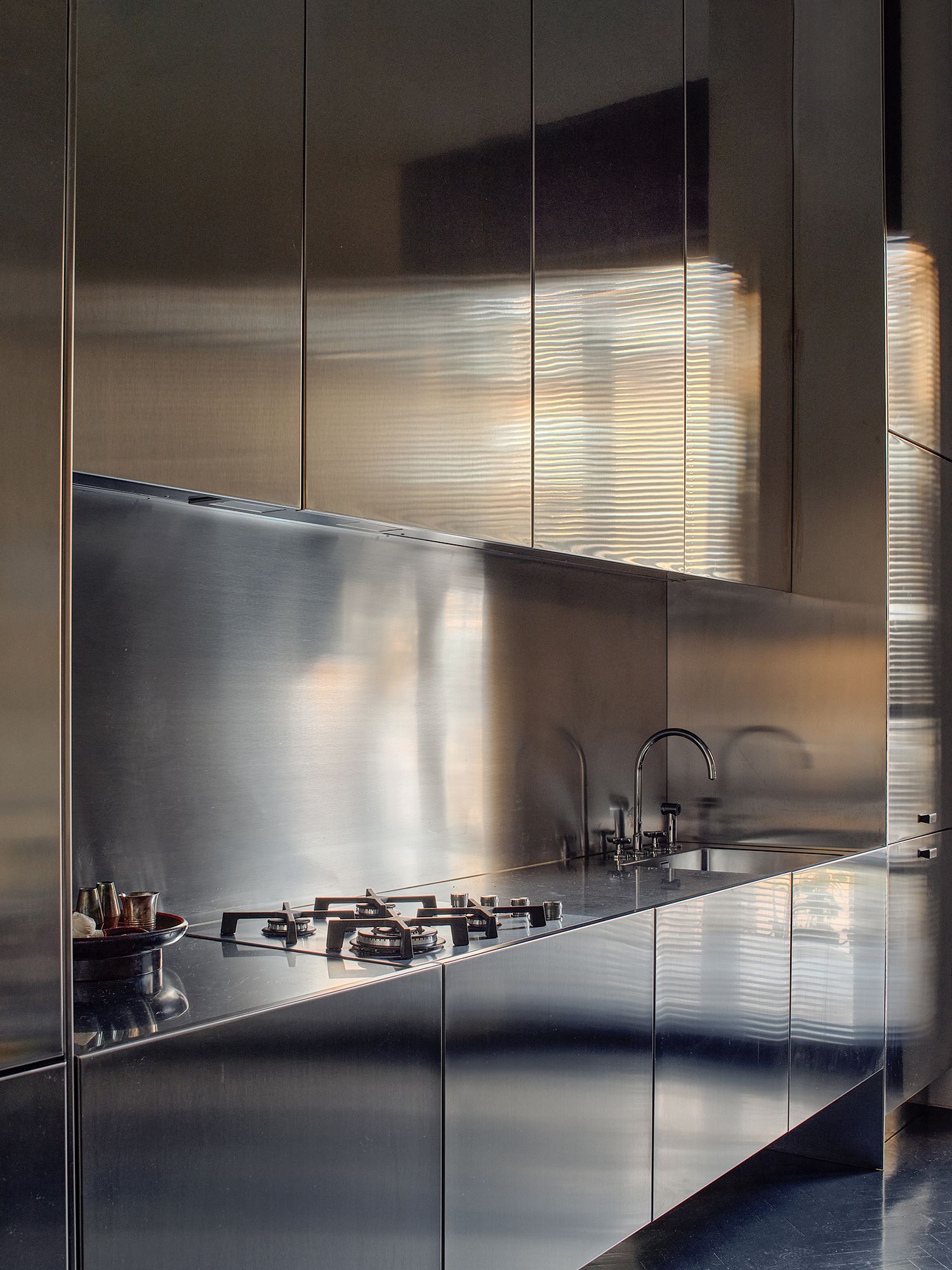 Weiche Lichtspiele entstehen wenn die Edelstahlküche das durchs Lamellenrollo gefilterte Sonnenlicht reflektiert