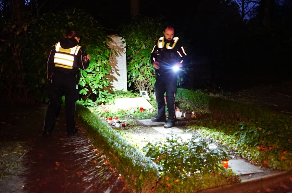 Polizisten leuchten mit Taschenlampe die Grabstelle aus