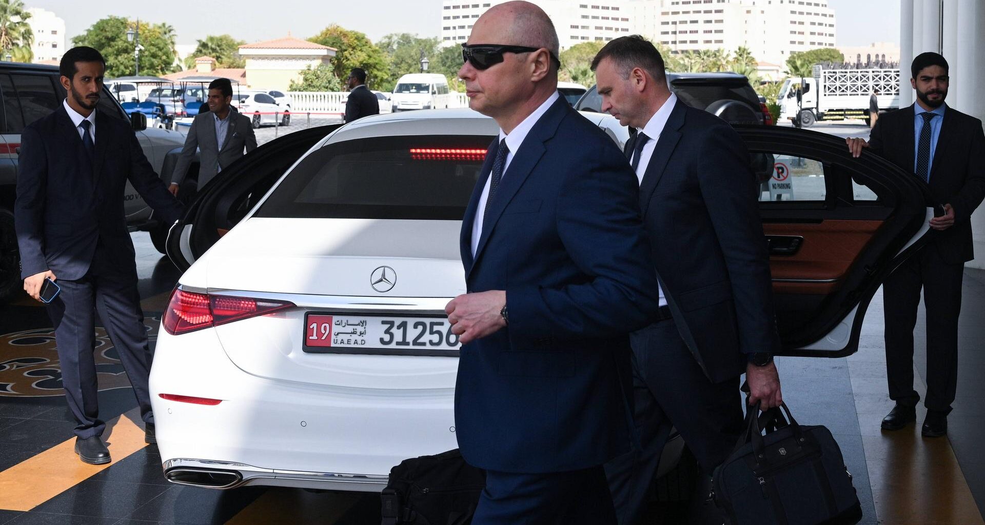 Die russische Delegation verlässt das Hotel in Abu-Dhabi zu Verhandlungen über den Ukraine-Krieg. Mehrere Männer in dunklen Anzügen stehen und gehen um ein weißes Auto herum.