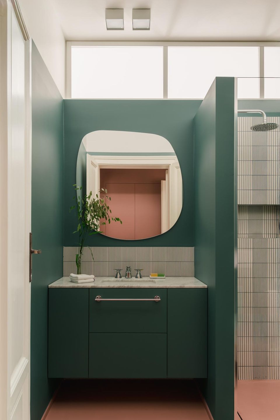 Ansicht des Waschbeckens und Anschnitt der Dusche mit asymmetrischem Spiegel und grüner Wand