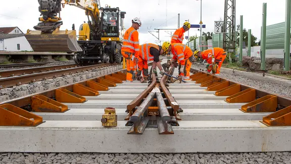Neue Schienen werden von Arbeitern in Schutzkleidung auf einem Gleisbett verlegt.