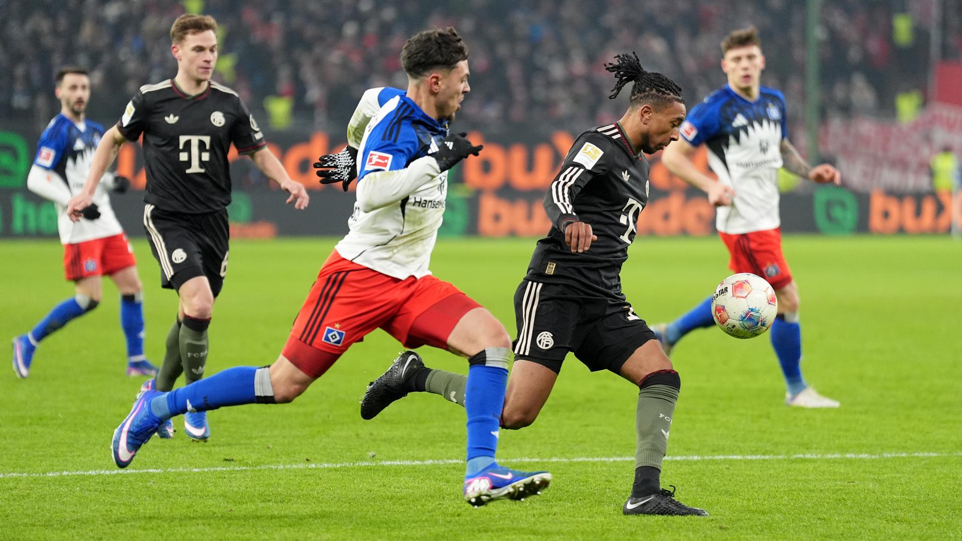 Das Bild zeigt zwei Fußball-Spieler in vollem Lauf beim Kampf um den Ball. In Hintergrund sind Mitspieler zu sehen, die das Geschehen beobachten. Das Bild zeigt zwei Fußball-Spieler in vollem Lauf beim Kampf um den Ball. In Hintergrund sind Mitspieler zu sehen, die das Geschehen beobachten.