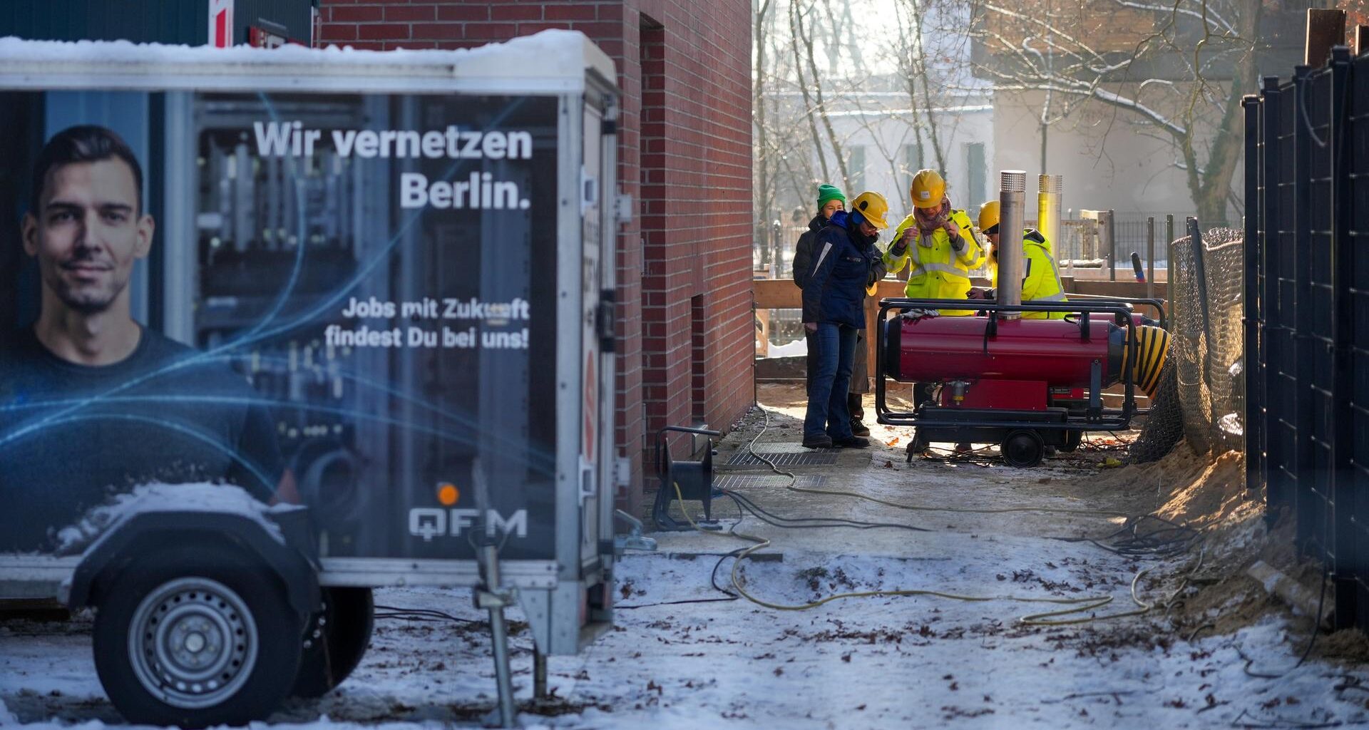 Mehrere Mitarbeiter des Umspannwerkes an der Argentinischen Allee stehen hinter einem Zaun nebeneinander. Im Vordergrund steht ein Anhänger mit der Aufschrift "Wir vernetzen Berlin".