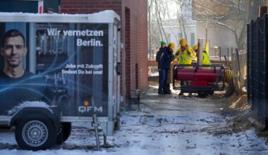 Mehrere Mitarbeiter des Umspannwerkes an der Argentinischen Allee stehen hinter einem Zaun nebeneinander. Im Vordergrund steht ein Anhänger mit der Aufschrift "Wir vernetzen Berlin".