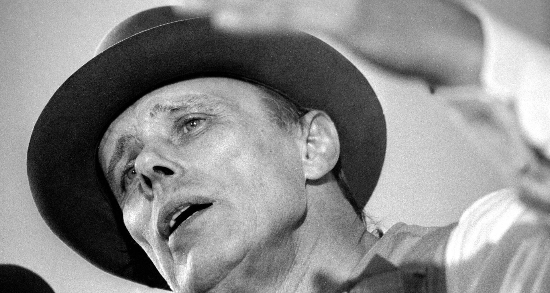 Der Künstler Joseph Beuys in Untersicht auf einem Schwarz-Weiß-Foto. Er diskutiert.