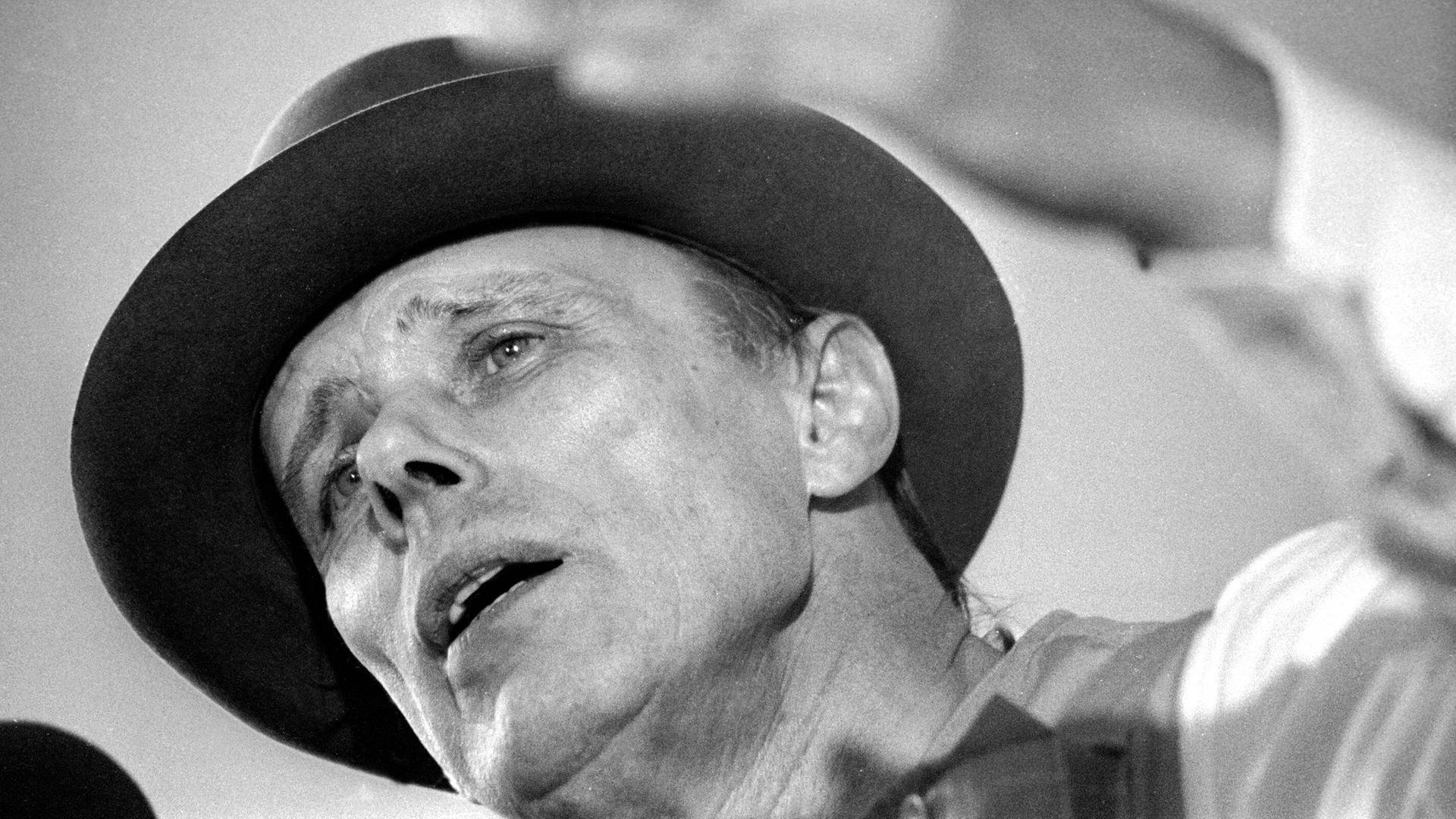 Der Künstler Joseph Beuys in Untersicht auf einem Schwarz-Weiß-Foto. Er diskutiert.